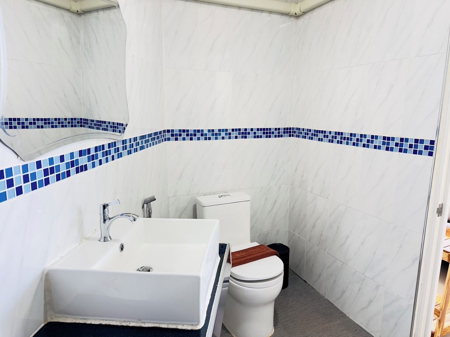 Un baño con lavamanos blanco, inodoro y una franja decorativa de azulejos azules.