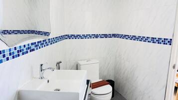 Un baño con lavamanos blanco, inodoro y una franja decorativa de azulejos azules.