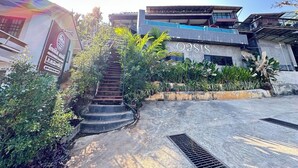 A building with a staircase leading to a balcony, surrounded by greenery. - Oasis Phamee (Mae Sai)