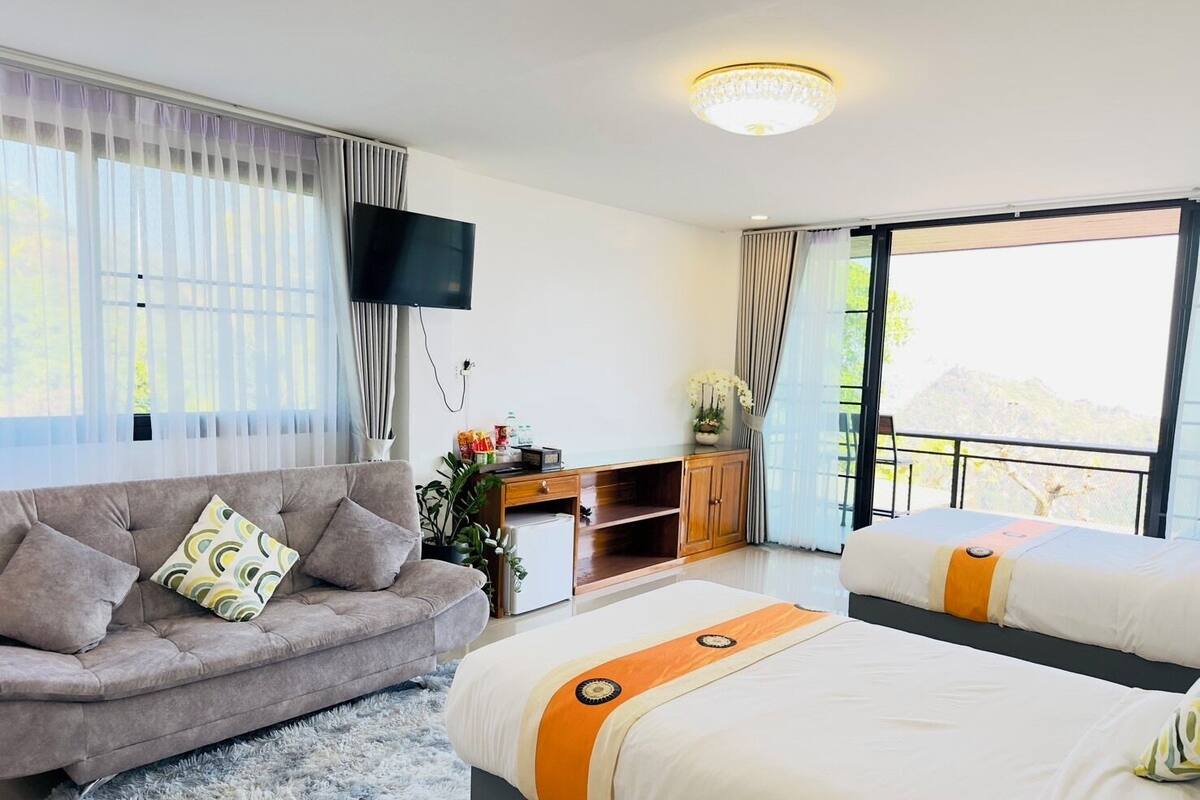 A modern hotel room with a sofa, a bed, a TV, and a balcony with a view.