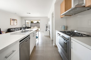 A modern kitchen with white cabinetry, stainless steel appliances, and a large window providing natural light. - Coastal Escape, Sun, Salt & Serenity (Ocean Grove)