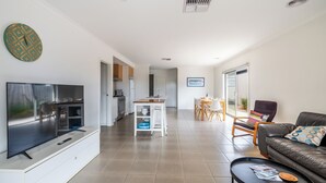 Een moderne woonkamer met een flatscreen televisie, een leren bank en een eethoek met een tafel en stoelen.