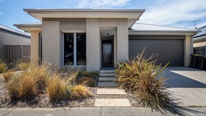 Een modern huis met een voordeur, een garage en een aangelegde tuin met inheemse planten.