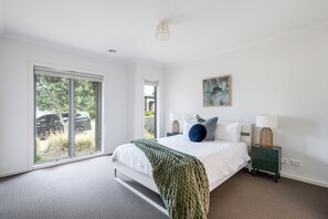 A modern bedroom with a large bed, a green nightstand, a white lamp, and a painting on the wall. - Coastal Escape, Sun, Salt & Serenity (Ocean Grove)