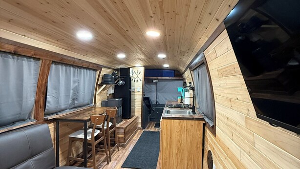 A compact RV interior with a kitchenette, seating area, and a small dining table. - Birch Bus in North Pole (North Pole)