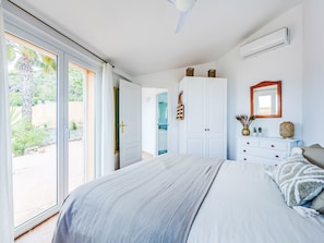 A bedroom with a bed, a wardrobe, a mirror, and a sliding glass door leading to a garden.