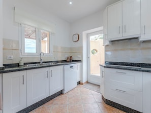 A kitchen with white cabinets, a granite countertop, a built-in dishwasher, and a window with a view.