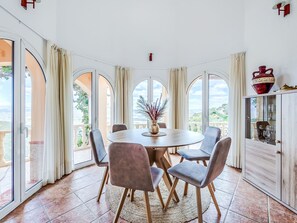 A dining area with a round table, chairs, and a view through large windows.