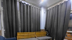 A room with a wooden bench, a blue chair, and grey curtains. - metroview rooms & celebration (New Delhi)