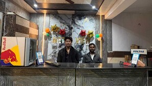 A reception desk with marble panels, a Red Bull refrigerator, and a ceiling fan. - metroview rooms & celebration (New Delhi)