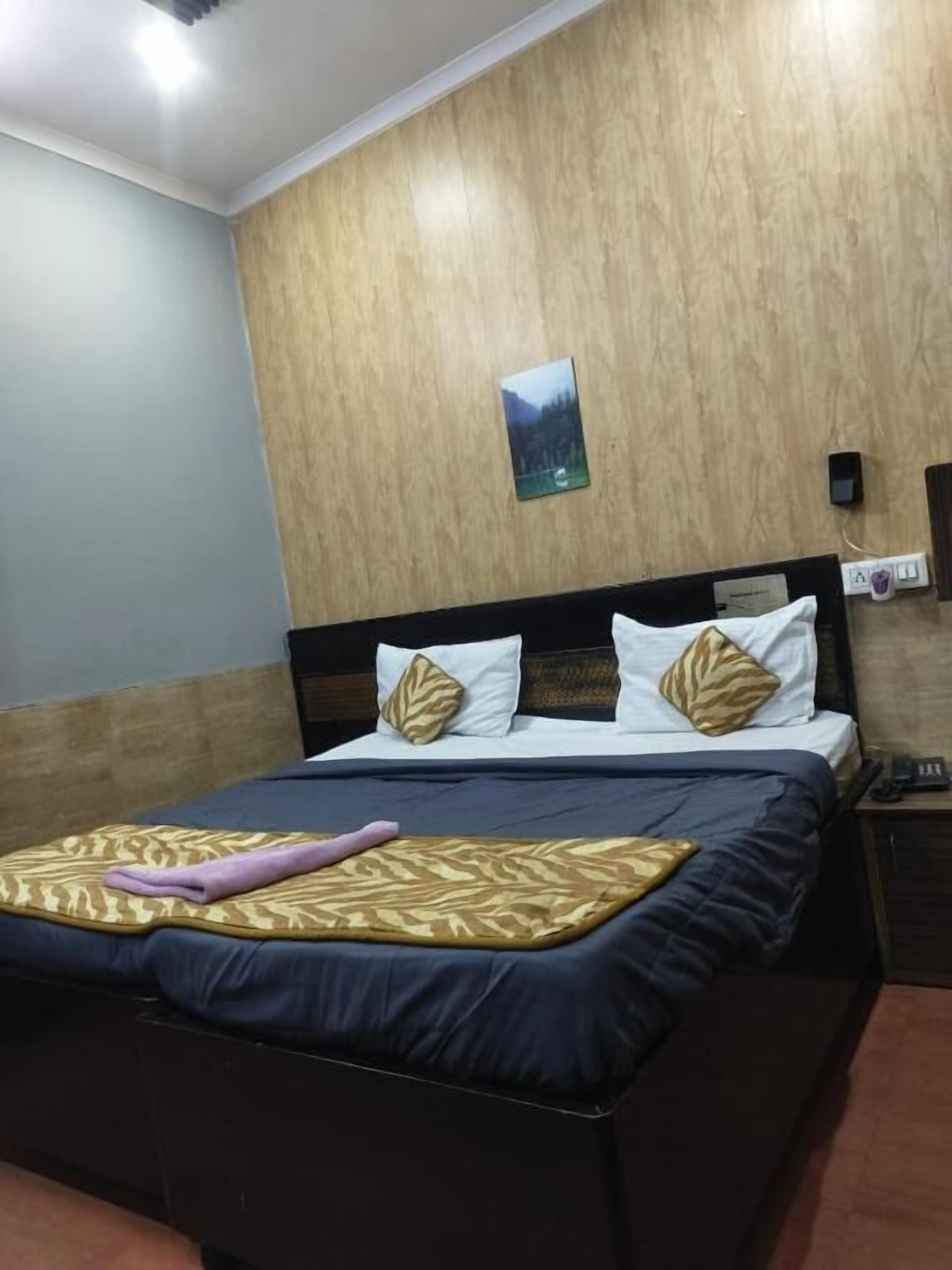 A hotel room with a wooden wall, a bed with patterned pillows, a bedside table with a phone, and a small picture on the wall.
