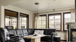 Una habitación con un sofá de cuero negro, una mesita y ventanas grandes con cortinas.
