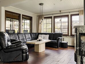 Ein Zimmer mit einer schwarzen Ledersofa, einem kleinen Tisch und großen Fenstern mit Vorhängen.