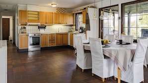 Una cocina con armarios de madera, horno de acero inoxidable y comedor con sillas blancas y una mesa.