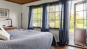 Un dormitorio con cama, escritorio, silla, ventana con cortinas y vistas al exterior.