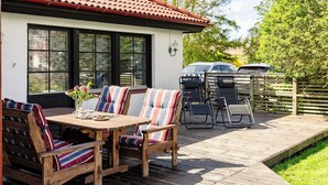 Un patio con mesa y sillas de madera, un pequeño jardín y un coche estacionado afuera.