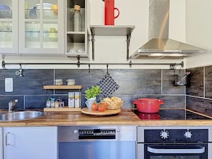 A modern kitchen with a stainless steel sink, a red pot on the stove, and a variety of spices and vegetables on the counter.