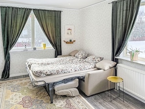 Une petite chambre à coucher comprenant un lit, un petit tabouret, un radiateur et une fenêtre avec des rideaux.