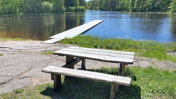 A wooden picnic table by a calm lake with a dock extending into the water. - Skolhuset by Interhome (Gullringen)