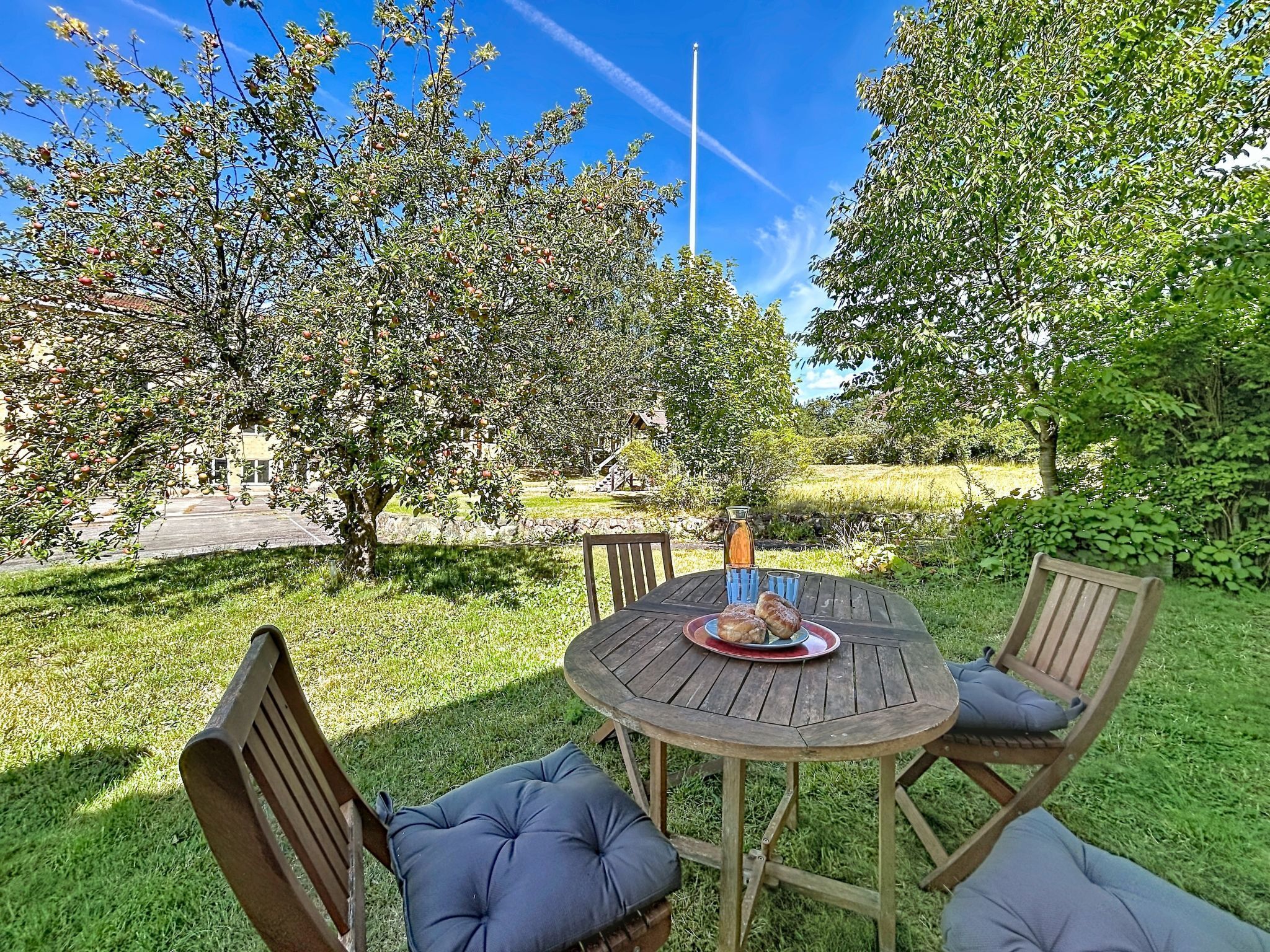 An outdoor seating area with a round wooden table and chairs, a bottle, and a plate with food.