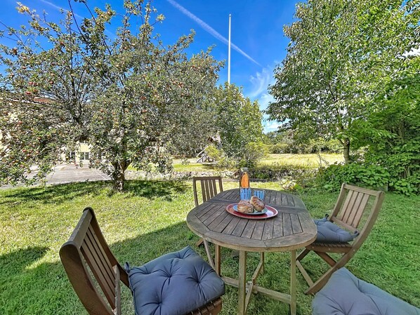 An outdoor seating area with a round wooden table and chairs, a bottle, and a plate with food.