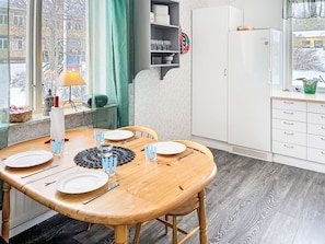 Un coin repas avec une table en bois dressée pour quatre personnes, un meuble blanc avec des étagères et une fenêtre donnant sur une rue enneigée.