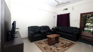 A living room with a flat-screen TV, two black leather sofas, a wooden coffee table, and a patterned rug. - Sanjana The Luxurious Family Stay 2 (Karkala)