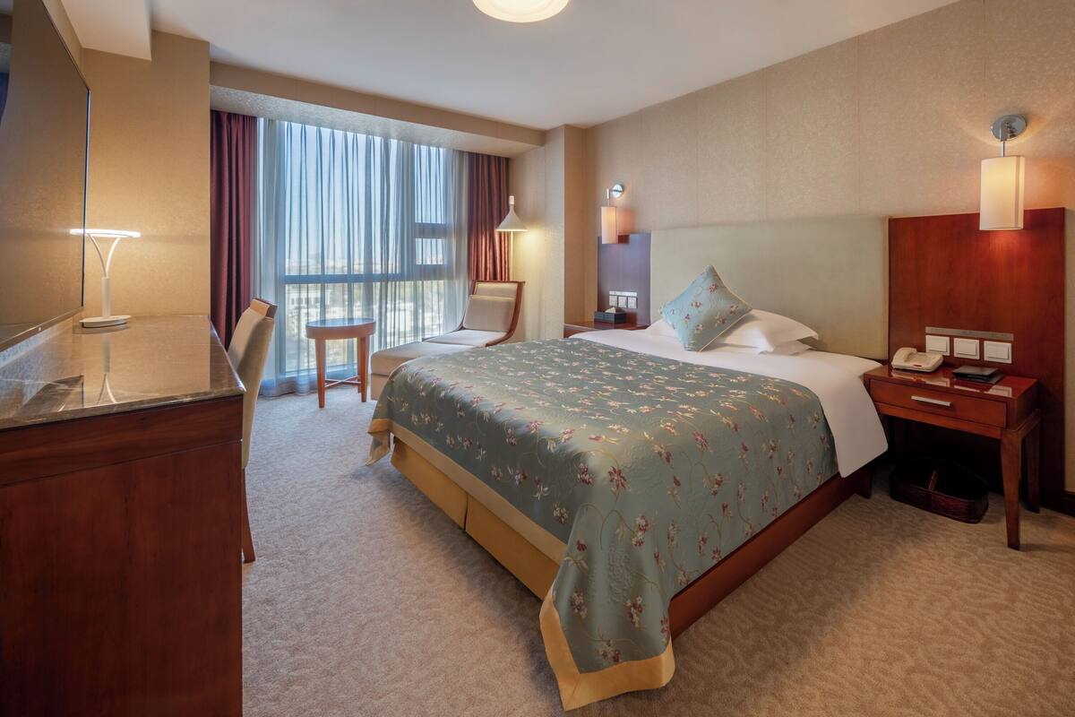 A hotel room with a large bed, a desk, a chair, a nightstand, and a lamp.