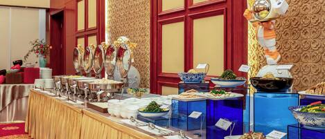 A buffet setup with various dishes and utensils, a decorative wall with a textured pattern, and a large window with a view of the outside.
