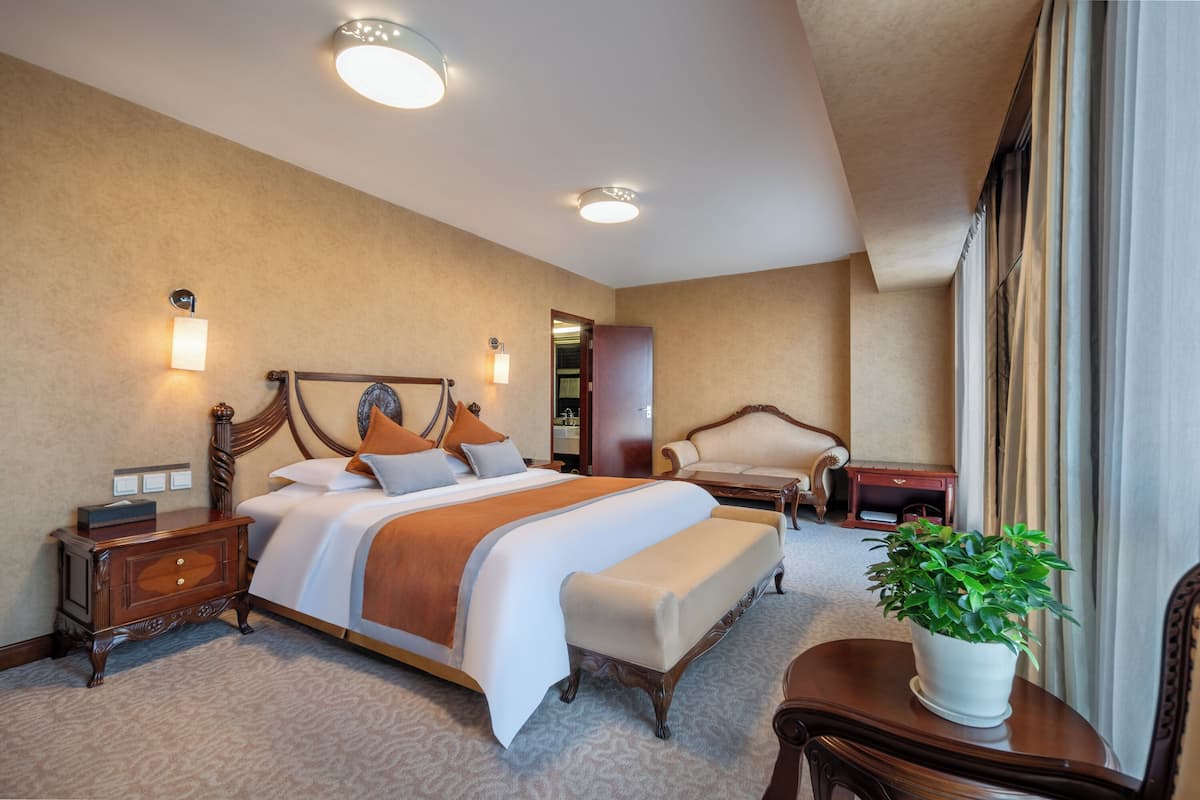 A hotel room with a large bed, bedside tables, a chair, a desk, and a potted plant.