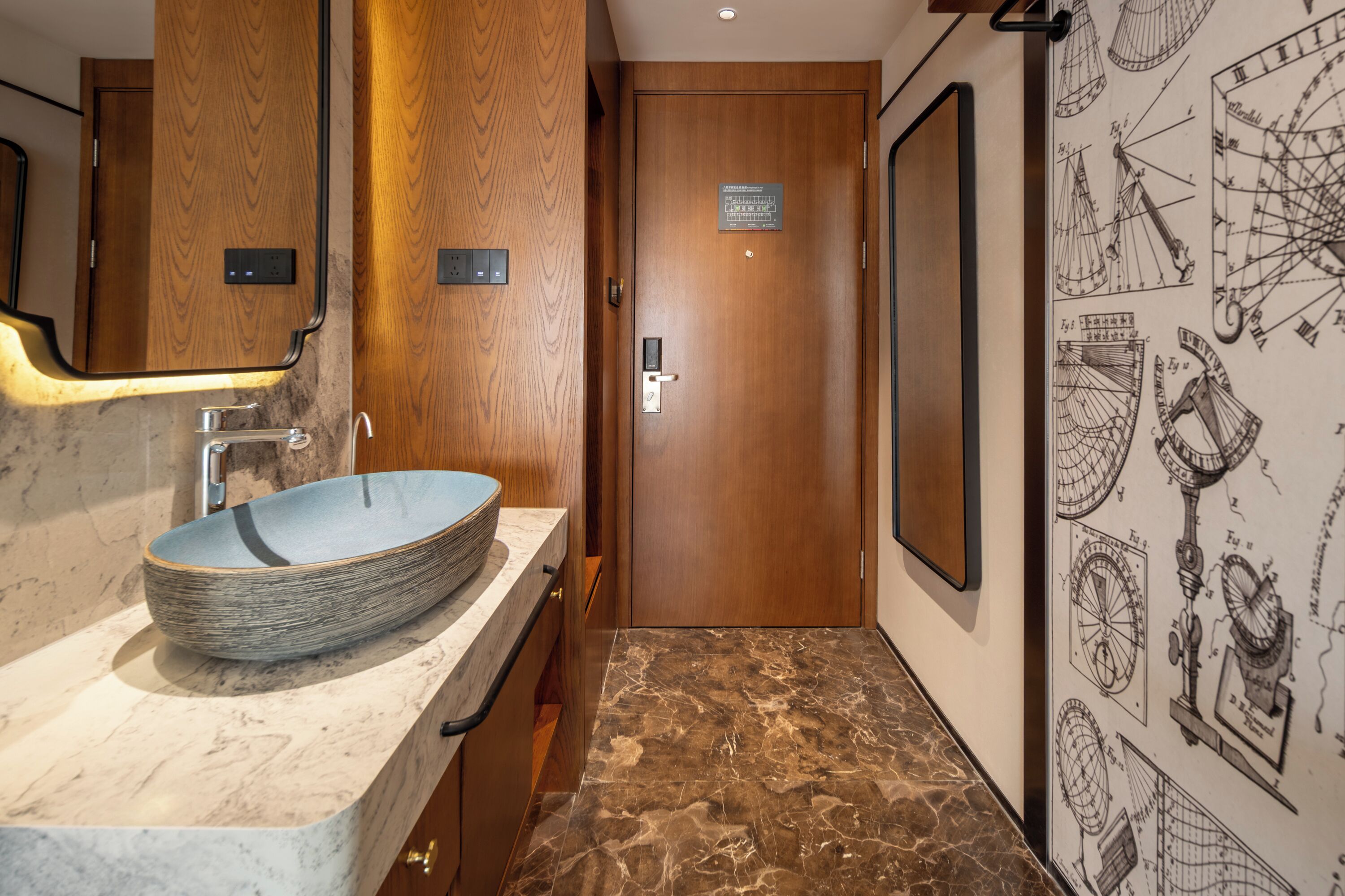 A bathroom with a wooden door, a marble sink, and a wall with nautical charts.