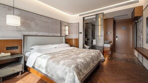 Ein modernes Hotelzimmer mit einem großen Bett, einem Nachttisch, einem eingebauten Kleiderschrank und einem Badezimmer mit Dusche und Toilette.