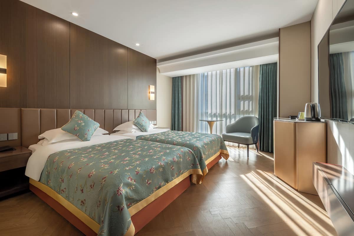 A hotel room with two beds, a desk, a chair, and a large window with curtains.