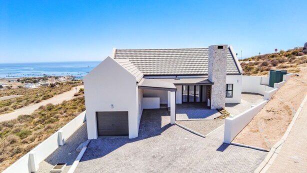 Una casa moderna con techo inclinado, chimenea de piedra y un camino de entrada pavimentado que conduce a un garaje.