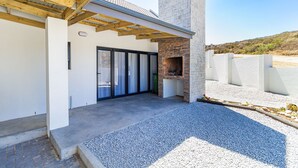 Un patio moderno al aire libre con suelo de hormigón, chimenea de piedra y una estructura de pérgola de madera.