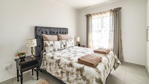 Un dormitorio con una cama grande, dos mesitas de noche, una lámpara y un ventanal con cortinas.