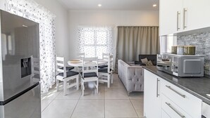 Una cocina moderna con armarios blancos, microondas integrado y un comedor con mesa y sillas blancas.