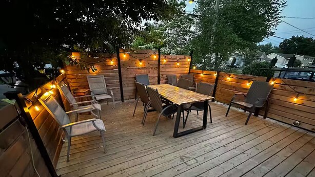 A wooden deck with a table and chairs, surrounded by string lights.
