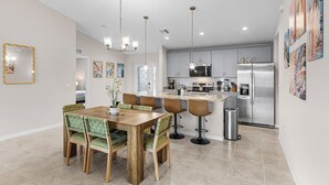 Una cocina moderna con armarios grises, electrodomésticos de acero inoxidable y una zona de comedor con mesa de madera y sillas tapizadas en verde.