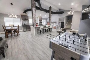 A modern living room with a foosball table, a dining area with a wooden table and chairs, and a kitchen area with a refrigerator and bar stools. - Villa in the HEART of town (Las Vegas)