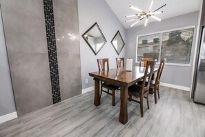 A dining area with a wooden table and chairs, two wall-mounted mirrors, and a ceiling light fixture. - Villa in the HEART of town (Las Vegas)