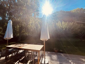 A wooden deck with a table and chairs, surrounded by trees and a view of a grassy area. - Charming and cozy cottage (Tranekær)