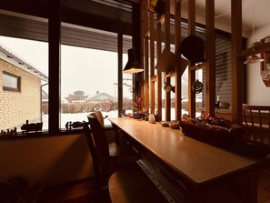 A dining area with a wooden table, chairs, and a view of a snowy landscape through large windows. - Charming and cozy cottage (Tranekær)