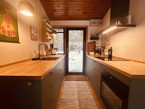A kitchen with wooden countertops, a sink, cabinets, and a window with a view of a snowy landscape. - Charming and cozy cottage (Tranekær)