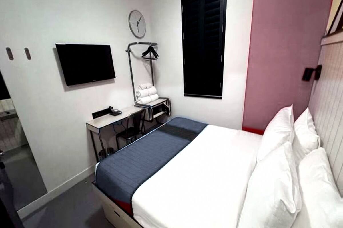 A hotel room with a bed, a TV, a desk, a chair, a towel rack, and a window.