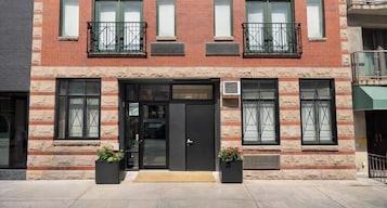 A two-story building with a black front door, large windows with black frames, and two black planters with flowers.