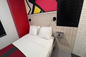 A bedroom with a bed, a nightstand, and a wall-mounted shelf.