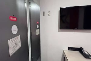 A room with a closed door, a television mounted on the wall, and a small table with a remote control.