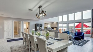 A spacious living area with a dining table set for six, a kitchen in the background, and large windows offering a view of the outdoors. - Panoramic Lake Belton Views: Home Near Marina (Belton)
