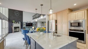 A modern kitchen with a marble island, stainless steel appliances, and a dining area with blue chairs. - Panoramic Lake Belton Views: Home Near Marina (Belton)